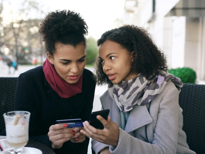 Two women comparing pay-later apps on a smartphone with a credit card